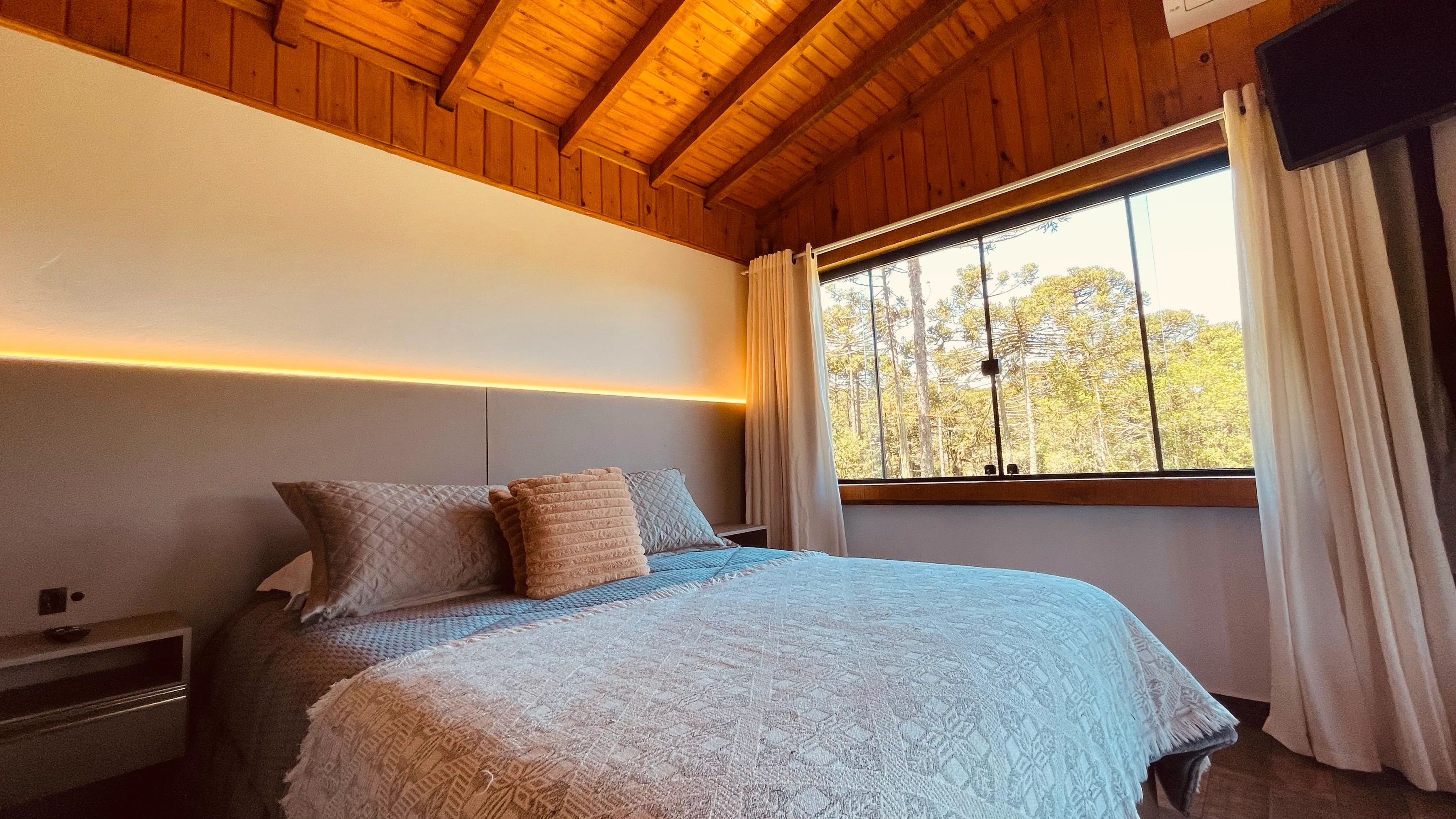 Quarto da cabana com cama de casal e janelas para o bosque