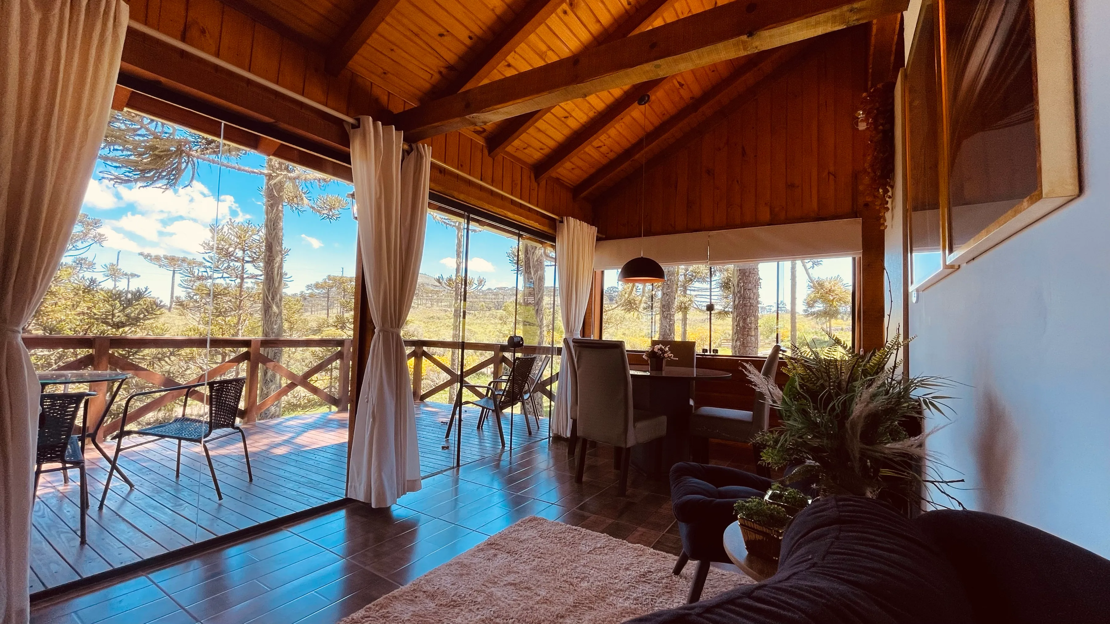Sala da cabana com janelas amplas e cortinas claras
