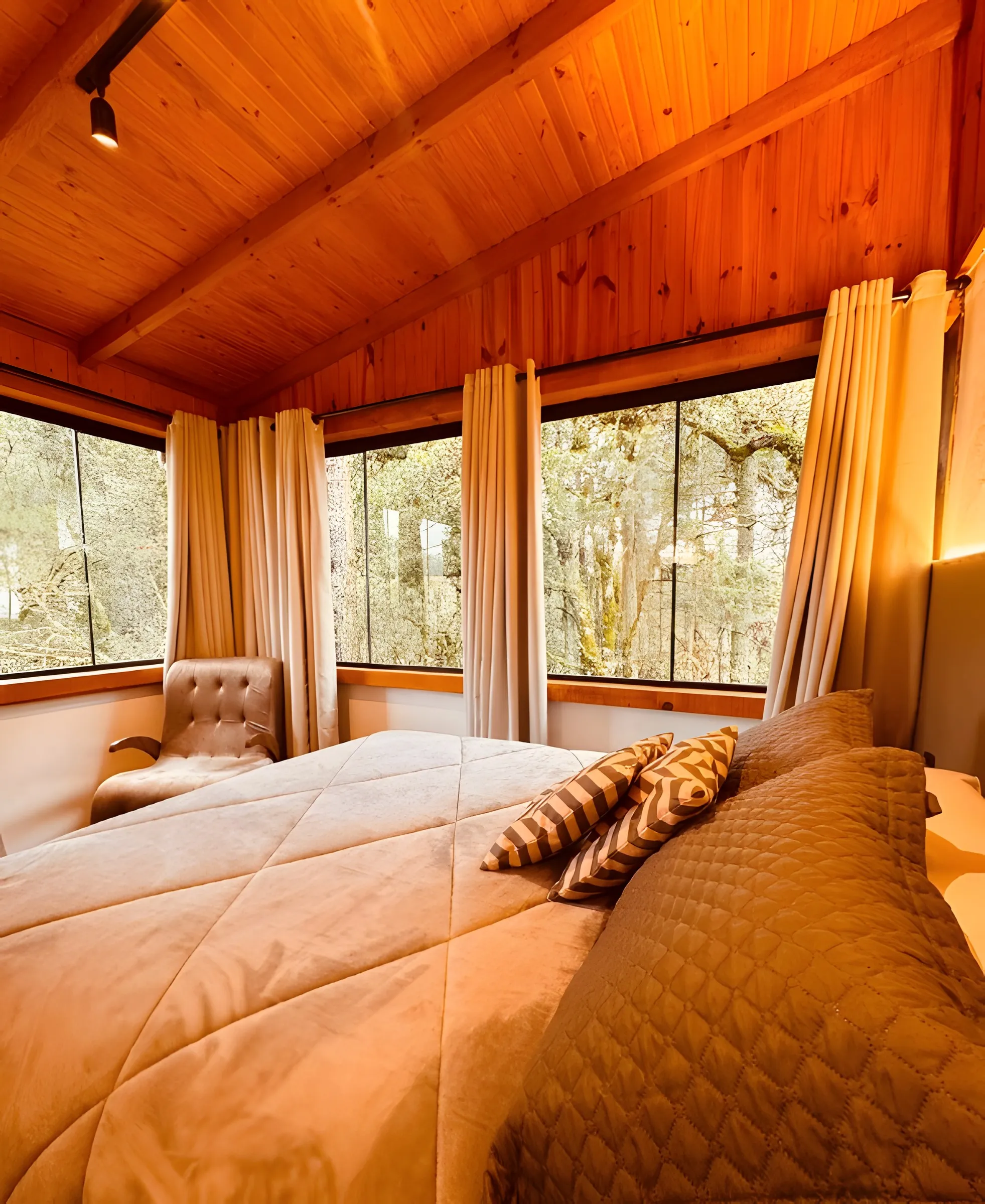 Quarto com cama de casal e janelas de madeira para o bosque